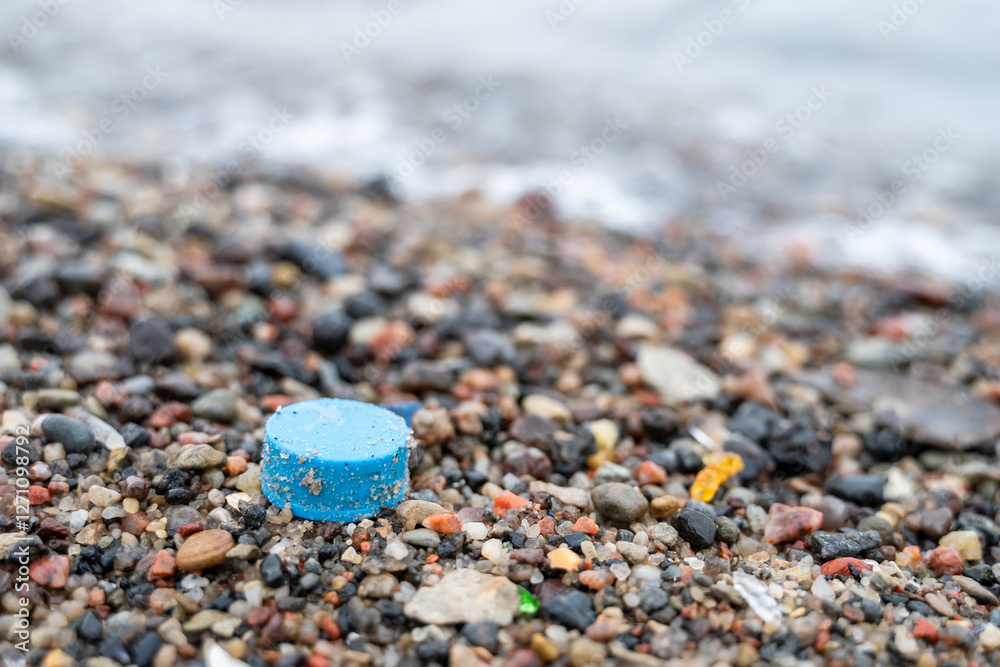 Plastic cap rests on sea beach with waves splashing behind, highlighting ocean pollution issue Plastic cap rests on sea beach with waves splashing behind, highlighting ocean pollution issue