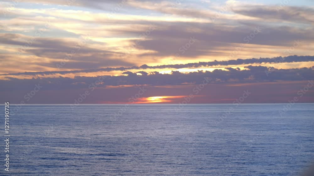 The sun rises over the ocean, casting golden light on the water. Dramatic clouds stretch across the sky, creating a colorful contrast with the deep blue sea in this breathtaking morning scene. The sun rises over the ocean, casting golden light on the water. Dramatic clouds stretch across the sky, creating a colorful contrast with the deep blue sea in this breathtaking morning scene.