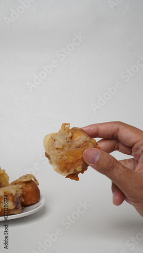 A hand holding a gehu, which is fried tofu filled with bean sprouts coated in wheat flour with a white background (isolated white). photo