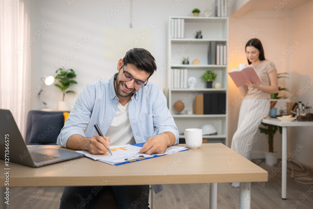 Portrait of a young freelancer smiling while working online via laptop at home with his girlfriend Portrait of a young freelancer smiling while working online via laptop at home with his girlfriend