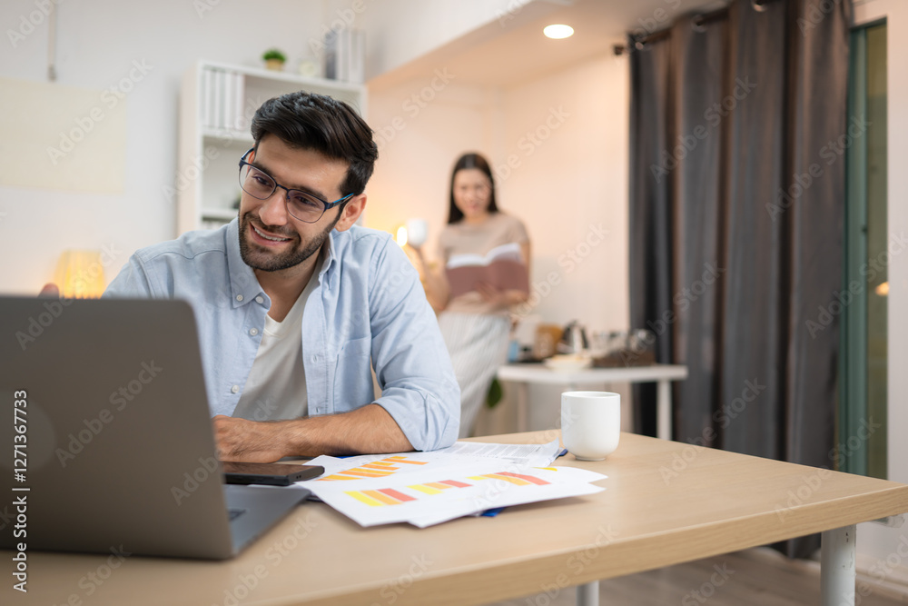 Portrait of a young freelancer smiling while working online via laptop at home with his girlfriend Portrait of a young freelancer smiling while working online via laptop at home with his girlfriend