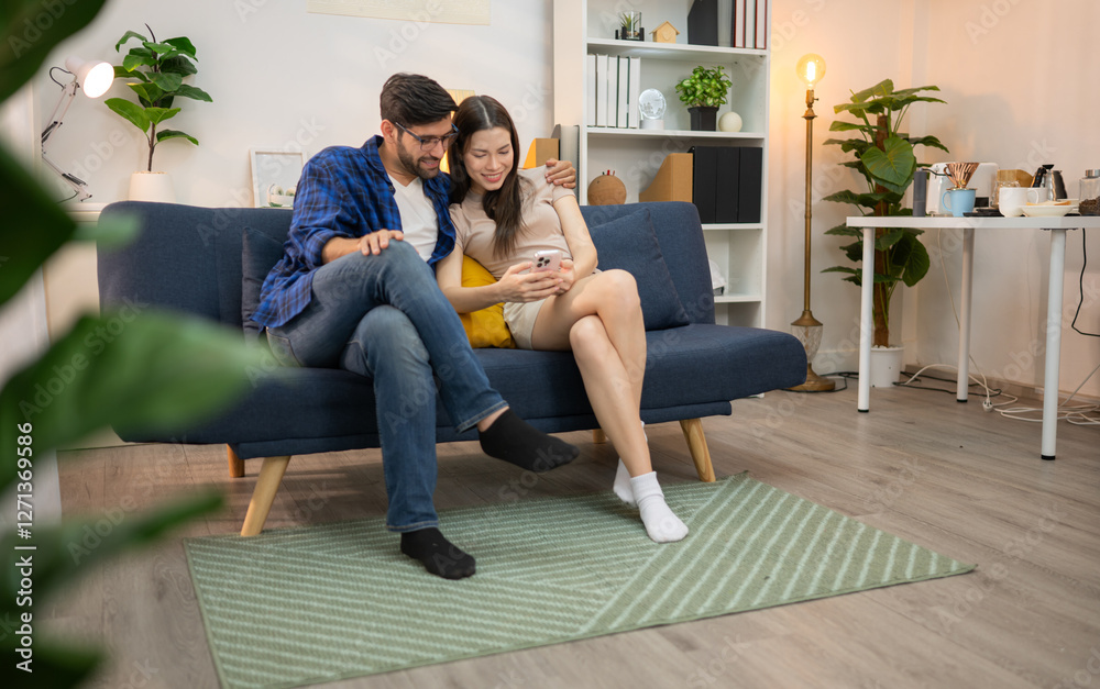 Obraz premium Young couple are smiling while relax and working online via laptop in living room at home