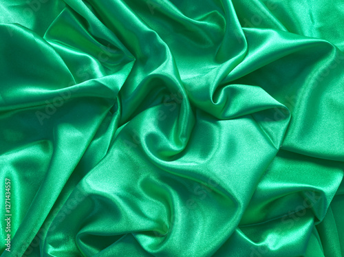 Elegant smooth green satin, silk fabric drapes. Luxurious cloth textile with liquid wave. Abstract green background or template. Fabric shiny glitter texture. Luxurious light green  background.	