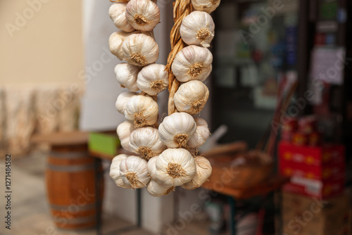 A close-up of a braid of garlic bulbs hanging outside a traditional market. The off-white bulbs with dried stems are woven together for easy storage and preservation photo