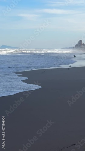Waves Gently Rolling on a Serene Beach with a Coastal City View