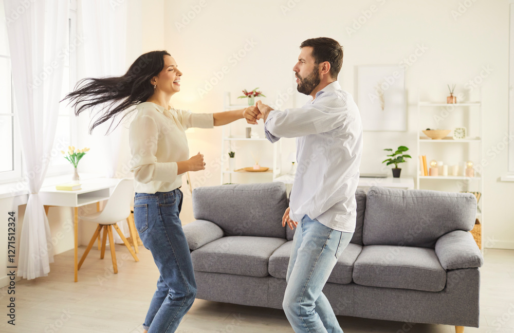 Fototapeta premium Two people dancing at home. Happy married couple having fun together. Young man and woman in casual clothes dancing in the living room. Family, love, romance, fun, leisure concept