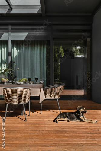 Foto Simple composition of terrace interior with table, chairs, brown tablecloth, tableware, big window, wooden floor, garden furnitures, vase with flowers and personal accessories