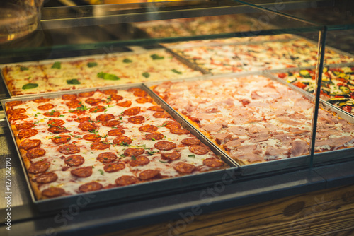 Authentic Italian pizza in a restaurant display window. Various pizzeria in glass window display. Focus on pizza with salami. View of slices of pizza in the restaurant