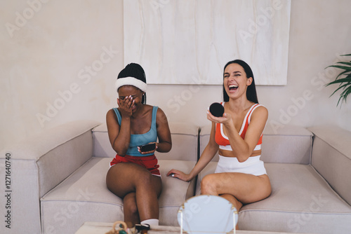 Biracial joyful friends sharing beauty morning ritual in bright minimalist interior, happy women in sportswear doing skincare routine together and laughing during natural moment of joy and bonding