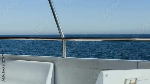 close-up of railings and seats on the upper deck of a boat swaying on the waves with a blue sea in the background
