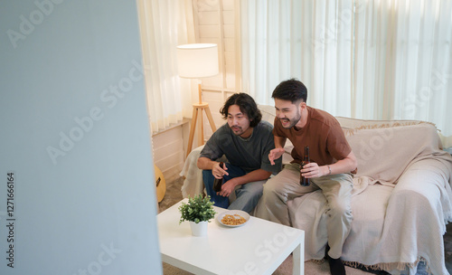 Wallpaper Mural Two Asian men drinking beer in a living room while watching football games on television intently with focused expressions. Two friends with soccer game. Friendship concept Torontodigital.ca