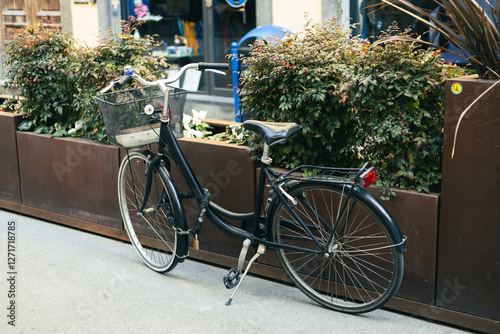 Fototapeta Naklejka Na Ścianę i Meble -  Vintage old bicycle parked in the urban narrow street. City transport concept. Lush green plants growing in pots near house