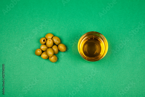 Groene olijven en een glas olijfolie op een groene achtergrond. De eenvoudige compositie benadrukt de natuurlijke oorsprong, pure smaak en gezonde eigenschappen van deze mediterrane producten. photo