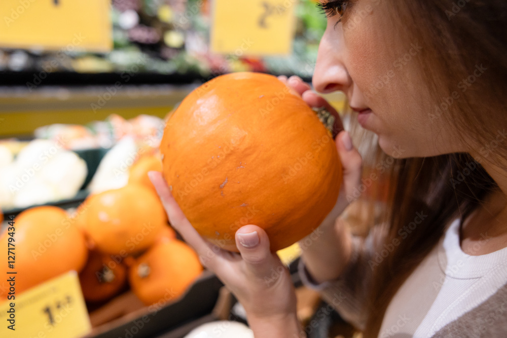 Fototapeta premium Woman smelling a fresh pumpkin in a supermarket. Concept of choosing high-quality ingredients, freshness, and mindful food shopping for a healthy lifestyle