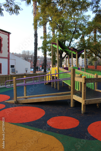Inclusive playground for children with functional diversity and physical disabilities. Ramp leading up to the play area with bright and fun colours. Rubber flooring with geometric shapes.