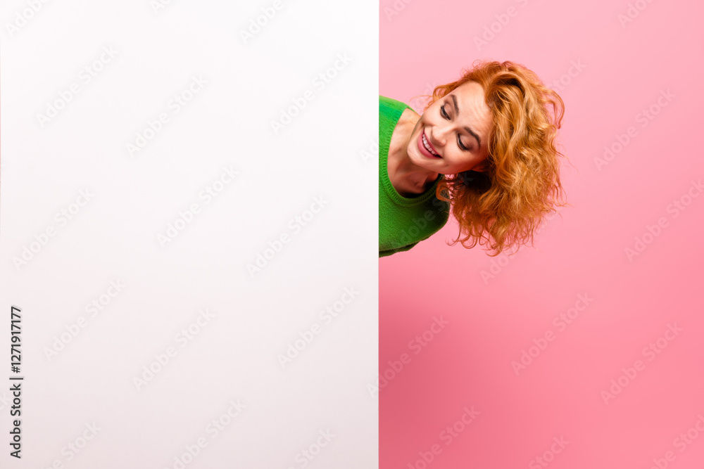 Φωτογραφία Cheerful woman with curly red hair in green jumper peeking out playfully against