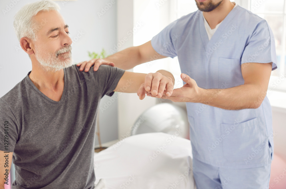 Obraz premium Man therapist massaging the arm of an old, senior male patient during a rehabilitation session in the clinic. This physiotherapy helps in the patient physical recovery and overall health.