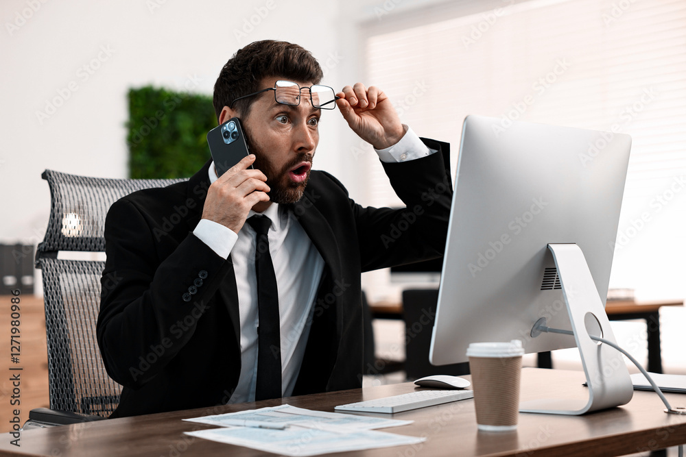 Man talking on smartphone while working at table in office Man talking on smartphone while working at table in office