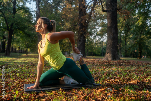 Fitness woman stretching legs doing pilates leg stretches exercises in outdoor park. Caucasian athlete exercising abductor hip flexor muscle in buttocks to relieve sports pain