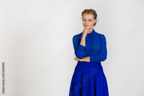 Рensive woman in a blue dress on a white background holds her hand under her chin and looks downward photo