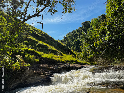 Rio cercado por montanhas e árvores sob um céu azul claro.