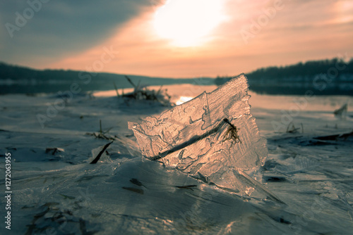 A toned photograph captures a piece of ice standing on the frozen surface of the river, with sunlight passing through it. Some parts of the river remain ice-free. photo