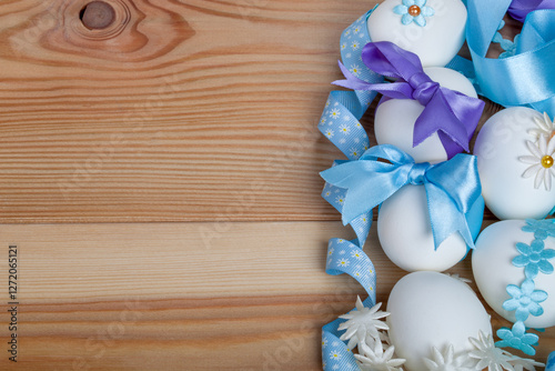 Several eggs are on a wooden table decorated with colorful beads, fabric butterflies, and stars for Easter. Some are adorned with blue ribbons.This festive scene is perfect for an Easter greeting card
