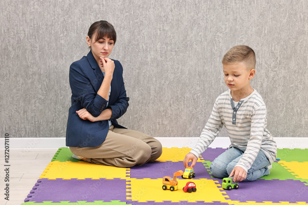Naklejka premium Psychologist observing little boy playing in autism treatment center