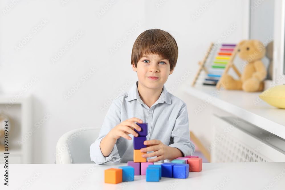 Boy building tower of colorful cubes at table indoors Boy building tower of colorful cubes at table indoors