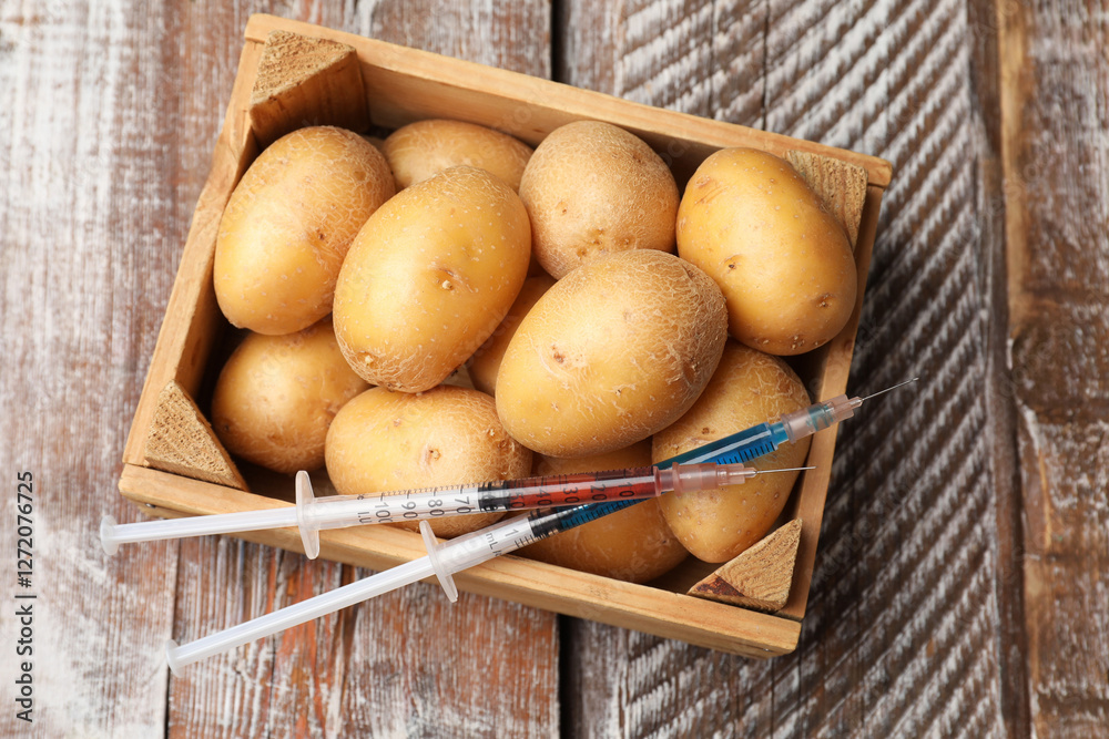 GMO concept. Potatoes in crate and syringes with liquid on rustic wooden table, top view GMO concept. Potatoes in crate and syringes with liquid on rustic wooden table, top view