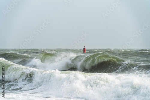 À Lesconil, sous un ciel couvert, de puissantes vagues aux reflets verts s’écrasent près d’une balise marine.
