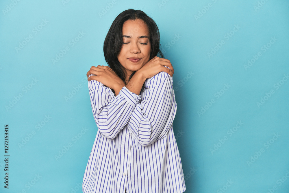 Fototapeta premium Filipina young woman on blue studio hugs, smiling carefree and happy.