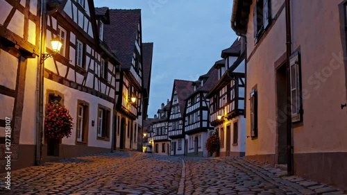 Quiet cobblestone street illuminated by warm streetlights at dusk