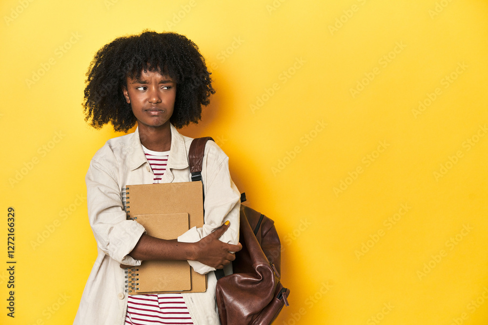 Studious teen girl with backpack and notebooks, yellow backdrop confused, feels doubtful and unsure. Studious teen girl with backpack and notebooks, yellow backdrop confused, feels doubtful and unsure.