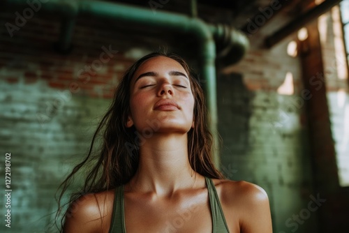 A young woman with eyes closed, sun-kissed skin, and long brown hair, in a rustic setting. photo