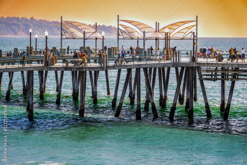 People walking along Redondo Beach Pier with a color sky and scenic background of the Palos Verdes Peninsula and dramatic sky People walking along Redondo Beach Pier with a color sky and scenic background of the Palos Verdes Peninsula and dramatic sky