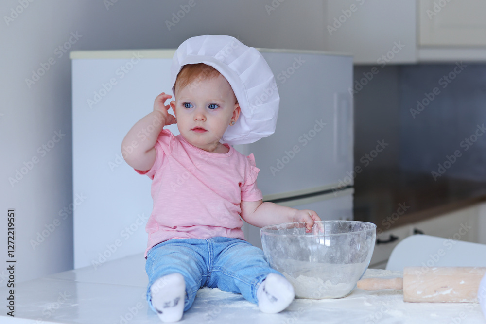 little girl in a white chef's hat rolls out dough on the kitchen table little girl in a white chef's hat rolls out dough on the kitchen table