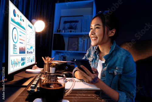 Smiling young beautiful asian creative looking on pc of profit of sales target report and writing on notebook for memo with planning invest new strategy market project at neon light night. Stratagem.