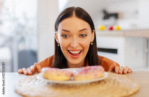 Hungry woman peeking out of table and starving to eat tasty donut, waiting for cheat meal moment, kitchen interior