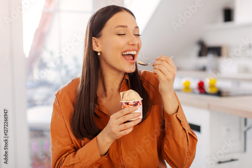 Attractive woman with tasty ice cream in kitchen, lady enjoy having cheat meal time and eating sweet dessert, space for text photo