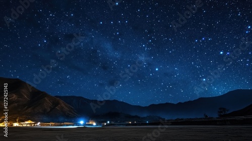 Starry night sky over mountain range and flatland with faint lights.