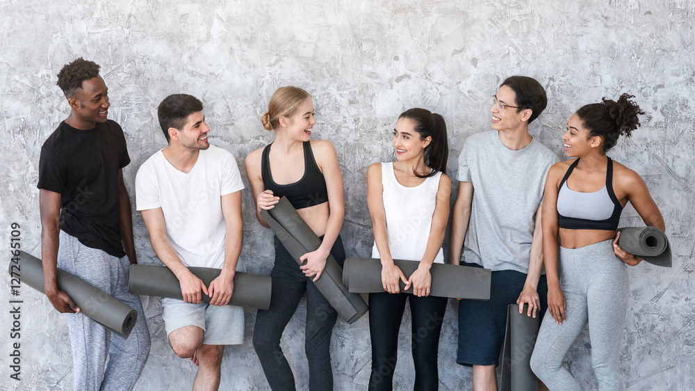 Fototapeta premium Healthy Lifestyle Concept. Group of sporty people with yoga mats resting after class near grey wall in fitness studio