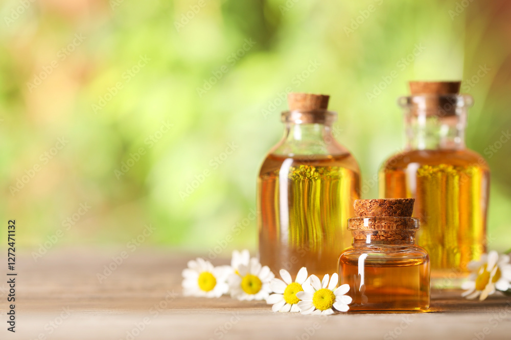 Bottles of essential oil and chamomile flowers on wooden table, closeup. Space for text Bottles of essential oil and chamomile flowers on wooden table, closeup. Space for text
