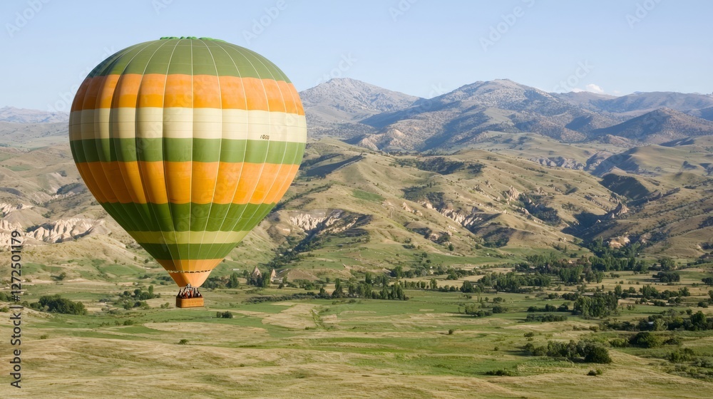 Obraz premium Kolorowy balon na ogrzane powietrze szybujący nad bujnymi zielonymi wzgórzami i górami o zachodzie słońca