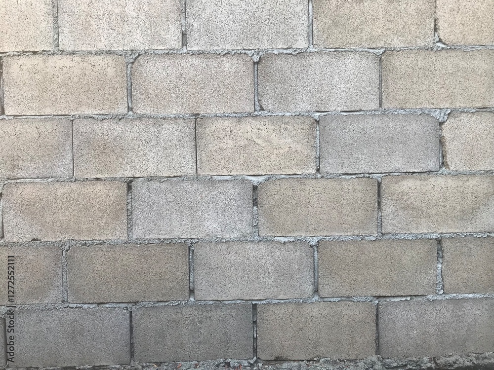 A close-up view of a concrete block wall.The blocks are rectangular and arranged in a regular pattern.The blocks are light gray with variations in shades. Mortar lines are visible between the blocks A close-up view of a concrete block wall.The blocks are rectangular and arranged in a regular pattern.The blocks are light gray with variations in shades. Mortar lines are visible between the blocks