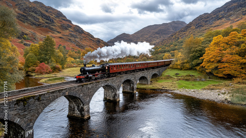 steam train crosses old stone bridge over deep river, surrounded by autumn trees © siraphol