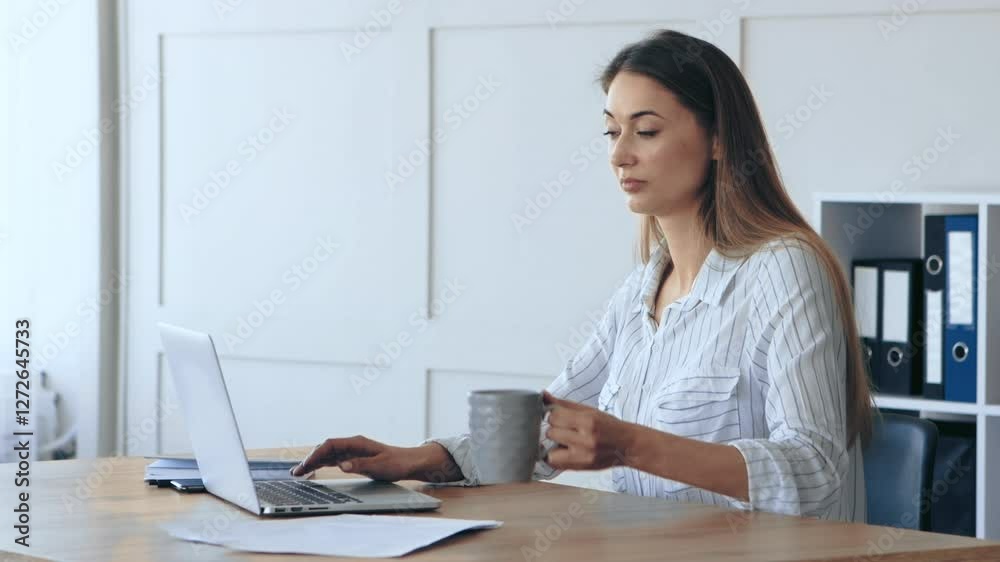 A woman sits at a wooden desk, focused on her laptop while holding a mug of coffee. The office is well-lit, featuring organized folders and a calm atmosphere conducive to productivity. A woman sits at a wooden desk, focused on her laptop while holding a mug of coffee. The office is well-lit, featuring organized folders and a calm atmosphere conducive to productivity.