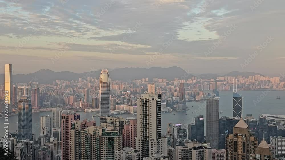 Hong Kong skyline at sunset with illuminated skyscrapers, Victoria Harbour, and distant mountains. The golden light enhances the city's architecture and urban landscape Hong Kong skyline at sunset with illuminated skyscrapers, Victoria Harbour, and distant mountains. The golden light enhances the city's architecture and urban landscape