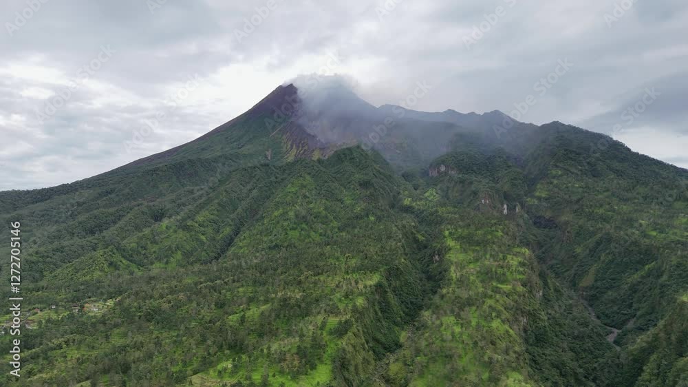 The most active volcano in indonesia, Mount Merapi. Green vegetation volcanic mountain emits smoke from the crater on the top. 4K Aerial drone footage. The most active volcano in indonesia, Mount Merapi. Green vegetation volcanic mountain emits smoke from the crater on the top. 4K Aerial drone footage.