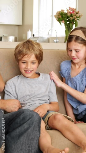 Father and daughter tickling son in the couch